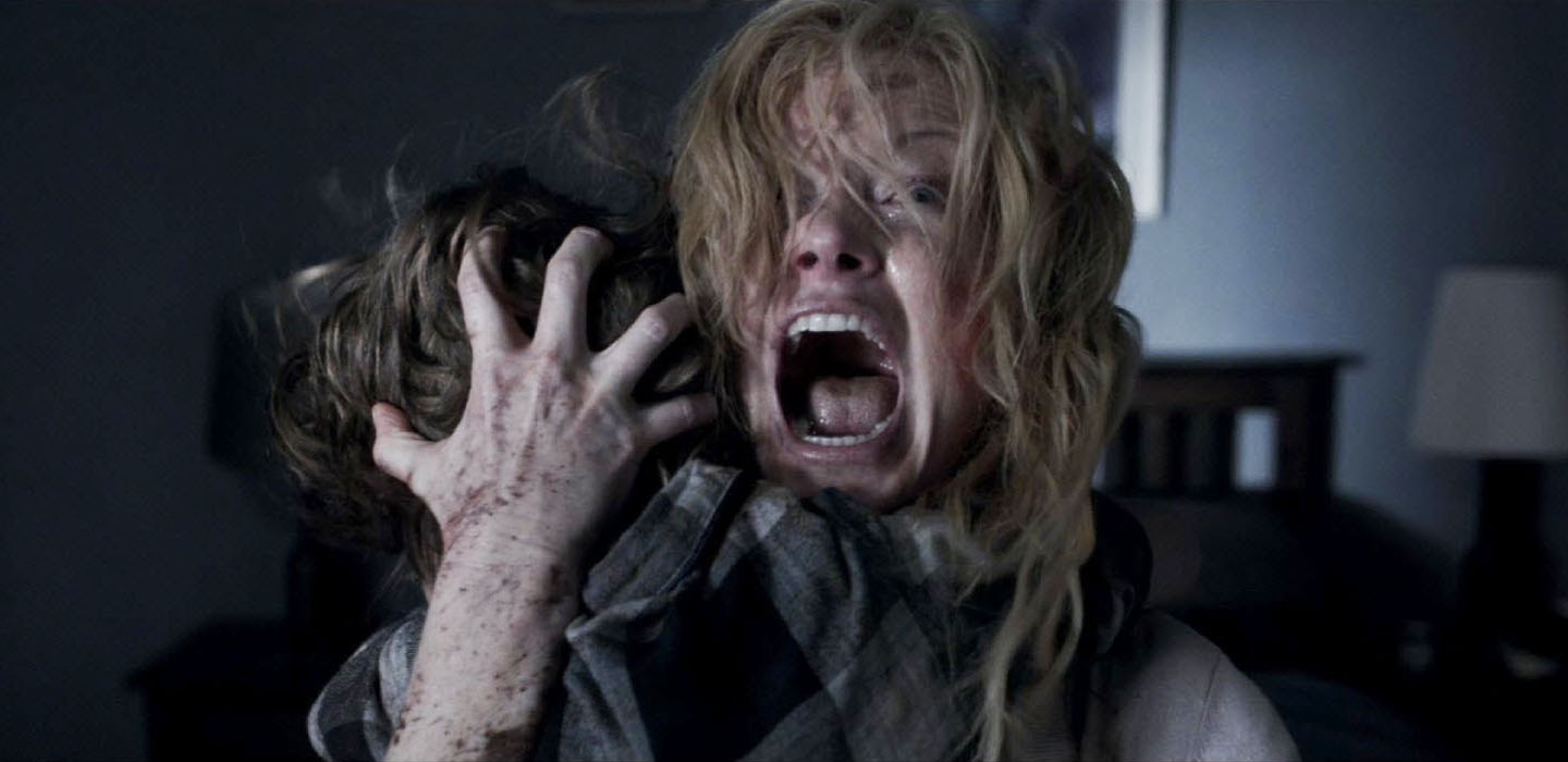 A frightened mother holding her young son close with her hand on the back of his head in The Babadook horror film