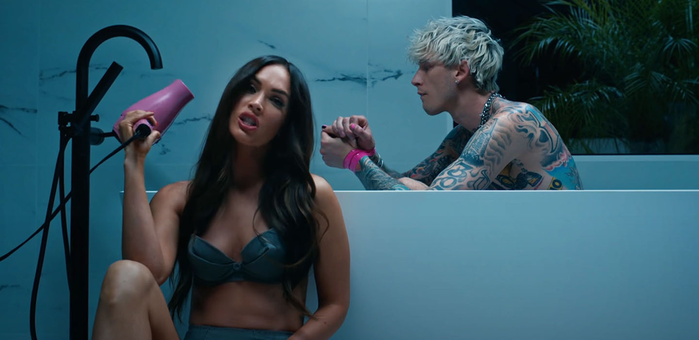 From music video "Bloody Valentine," actress Megan Fox sits by the bathtub with a blow dryer in hand while rapper Machine Gun Kelly is sitting inside the tub.