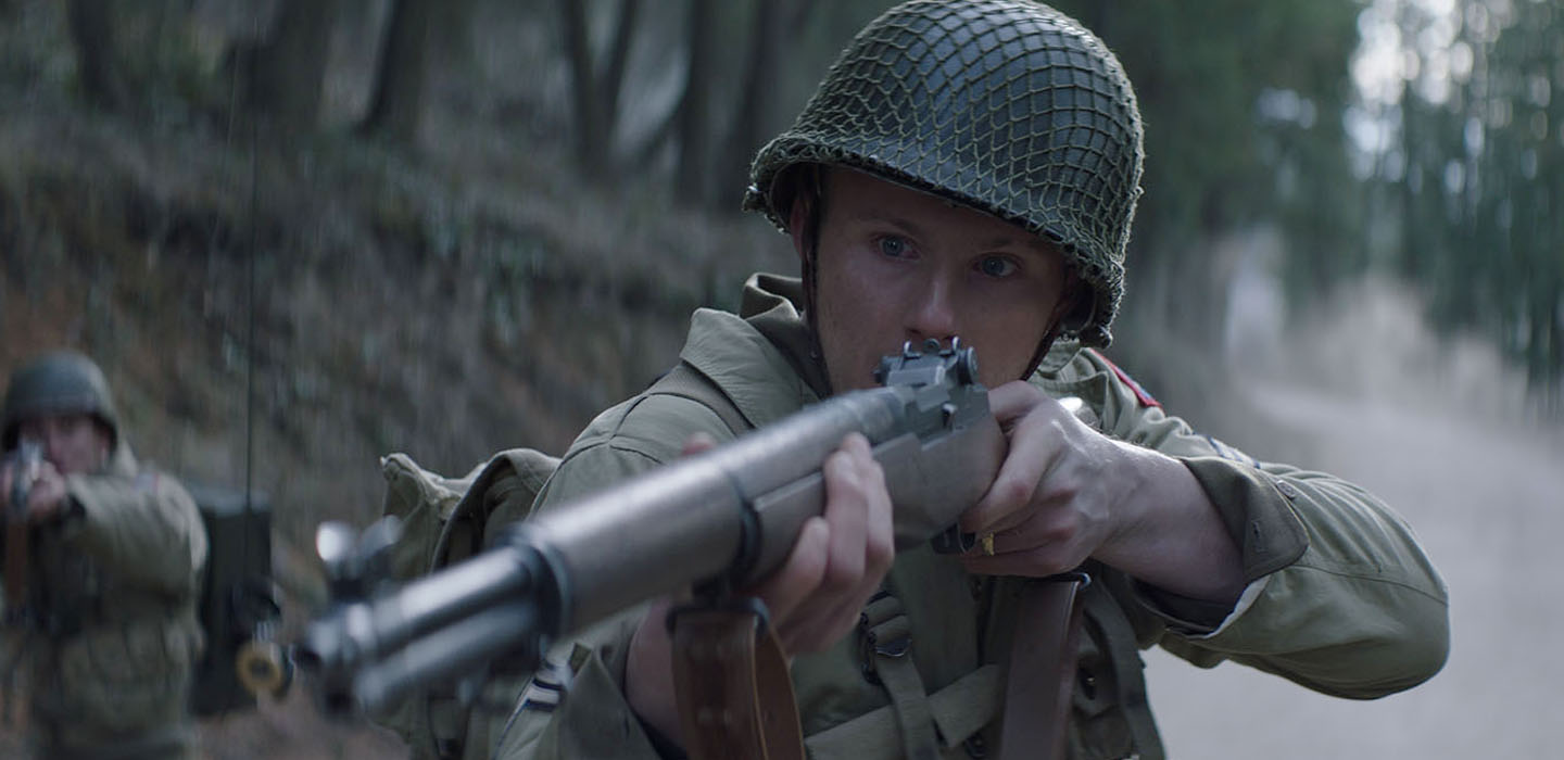 Canadian actor, Alexander Ludwig as an american soldier, pointing a rifle at the enemy in this publicity photo for RECON, a 2019 movie