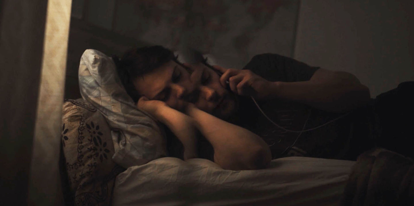 Actor, Alexander Horner is laying in bed holding his mobile phone in this publicity photo from Dedalus indie film