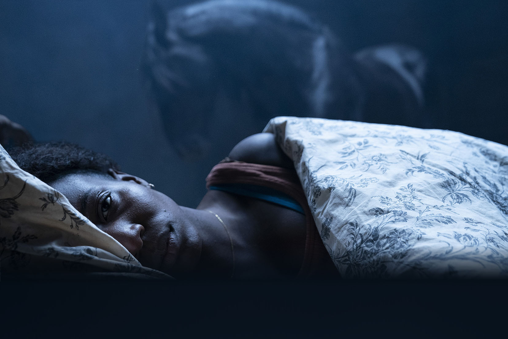 Actress Tamara Lawrence is laying in bed, facing the camera, and looking nervous in horror film, Kindred.